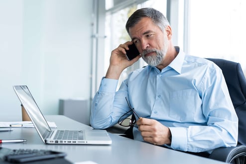 A man working on a laptop while talking in the phone